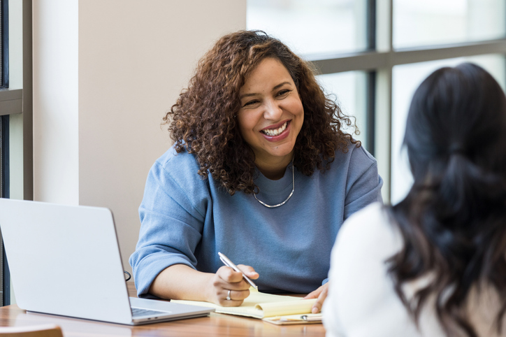 An Accessibility advisor talking with a student at a desk while taking notes.